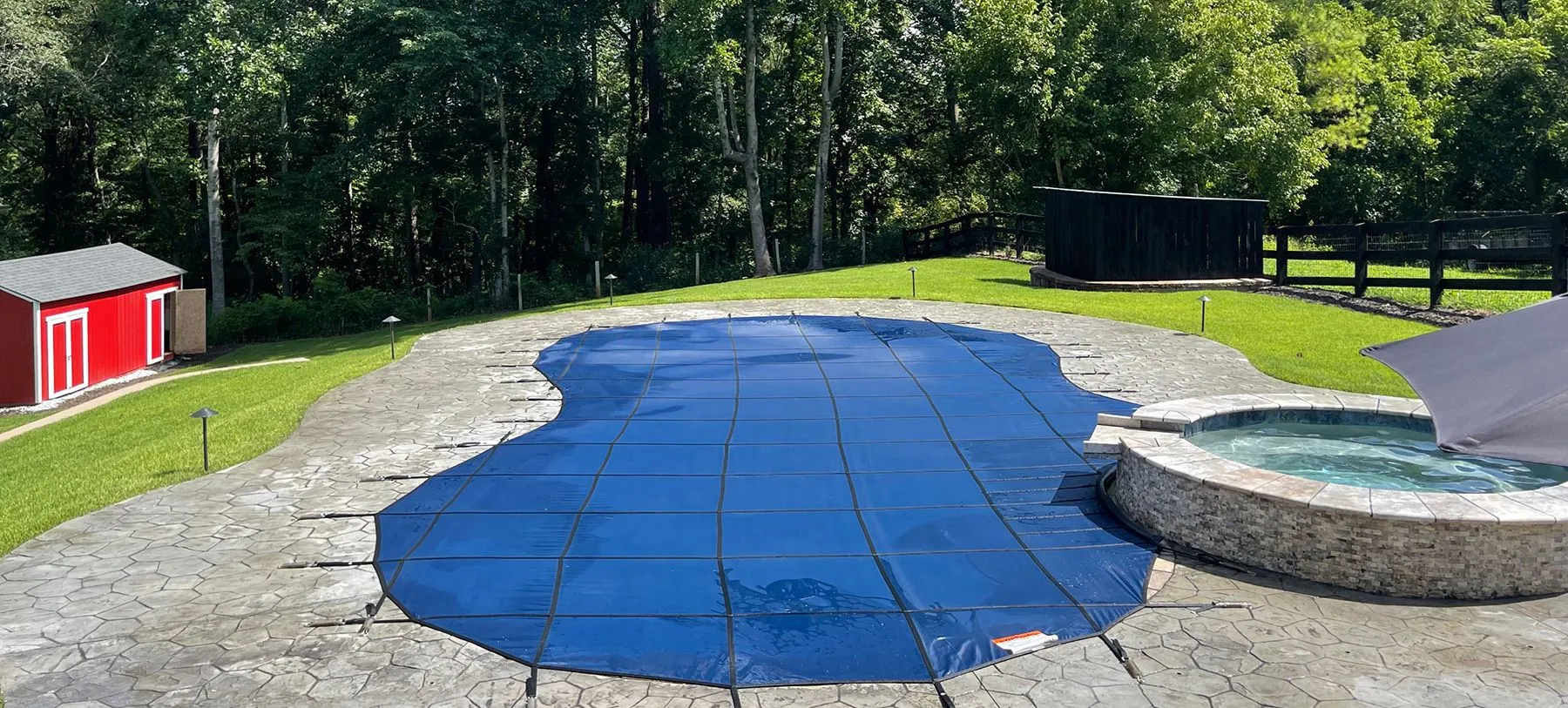 A kidney shaped swimming pool with blue safety cover and a hot tub.