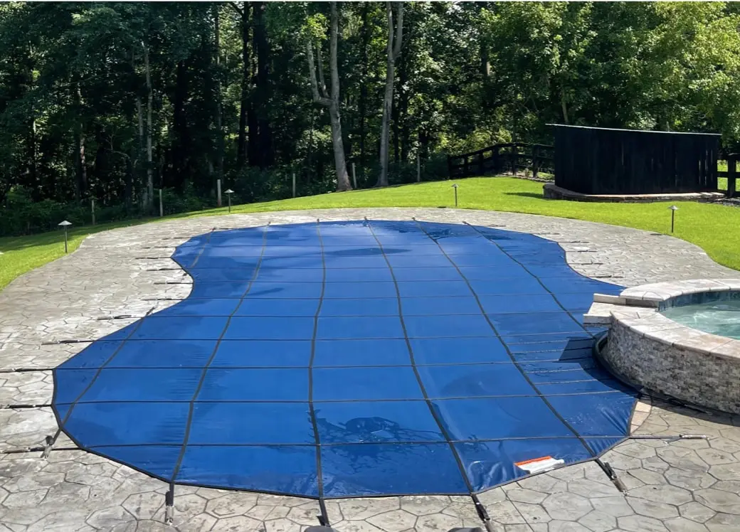 A kidney shaped swimming pool covered with a blue safety cover.