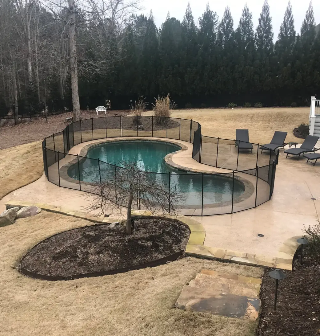 A kidney shaped pool with black fencing in the middle of a forest.
