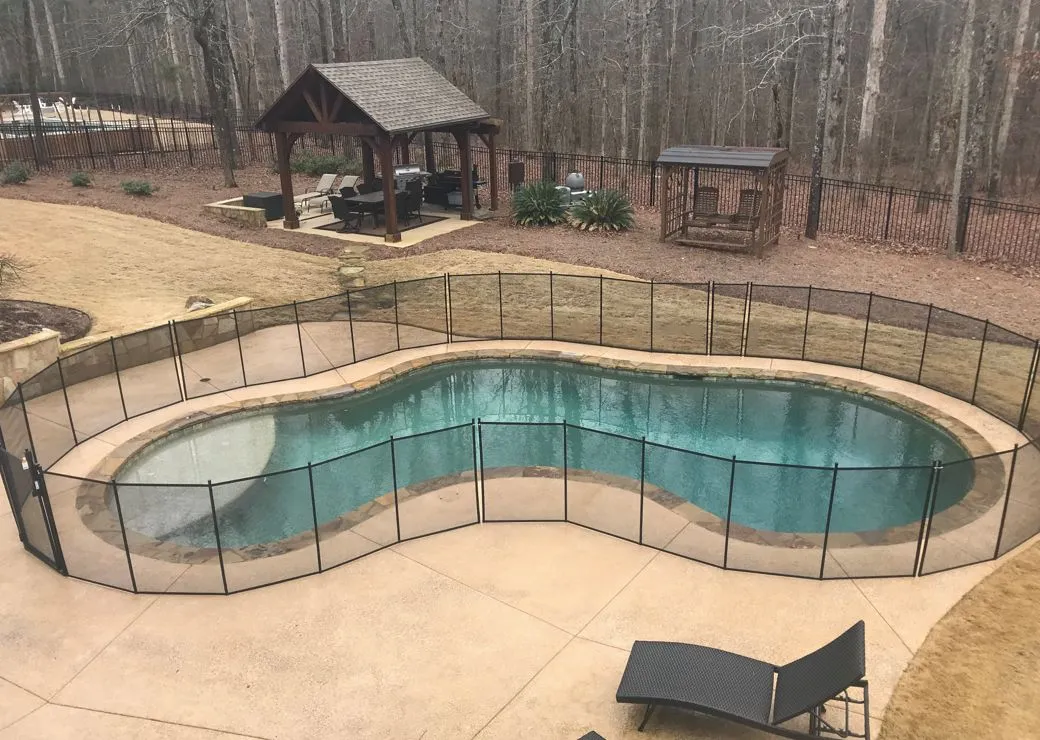 A kidney shaped swimming pool with black pool fences surrounded by a forest in Fulton County.