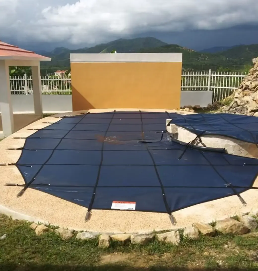 A kidney shaped swimming pool with a hot tub. Both are covered with a navy blue safety cover.